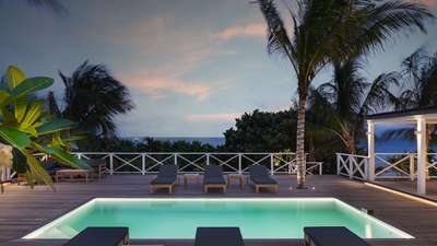Serene private swimming pool and wooden deck at dusk, featuring plush loungers and breathtaking ocean views in Toiny.