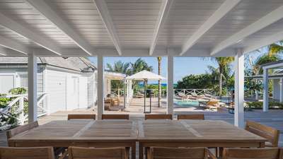 Covered outdoor dining area at Citron Vert Estate featuring a large teak table, wooden deck, and stunning oceanfront views.