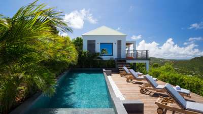 Beautiful white villa exterior, heated pool, and wooden deck with sun loungers at Villa Clementine, St. Barths.