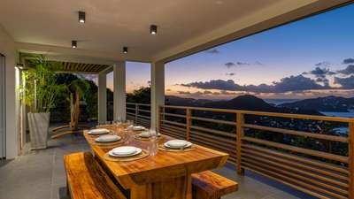 Al fresco dining on the covered terrace of Villa Clementine, featuring a wooden table and breathtaking sunset ocean views.