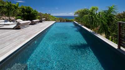 Glistening heated infinity pool and elegant wooden terrace with comfortable daybeds, showcasing stunning Caribbean sea views.