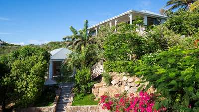 Elegant exterior of Villa Coco Rock featuring natural stone walls, wooden accents, and vibrant tropical hillside gardens.