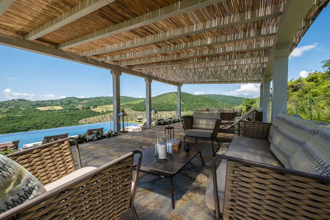 Elegant covered outdoor lounge with woven furniture and stone floors overlooking the infinity pool and Chianti hills.