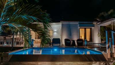 Cozy Amancaya's illuminated infinity pool by night, featuring a wooden deck, tropical palms, and elegant modern villa design.