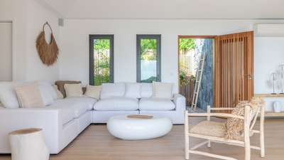 Tranquil living area with a white sectional, natural wood accents, and woven decor, opening to a serene tropical garden.