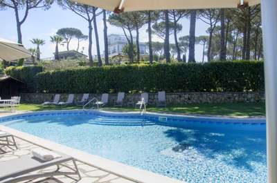 Stunning private swimming pool at Villa Dodola, surrounded by manicured hedges, tall pines, and comfortable sun loungers.