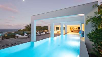 Illuminated 17-meter heated pool framed by elegant architectural arches, offering breathtaking ocean views at night.