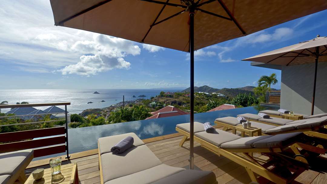 Relax on the wooden deck by the 15-meter heated infinity pool at Villa Edunia, offering panoramic ocean and harbor views.