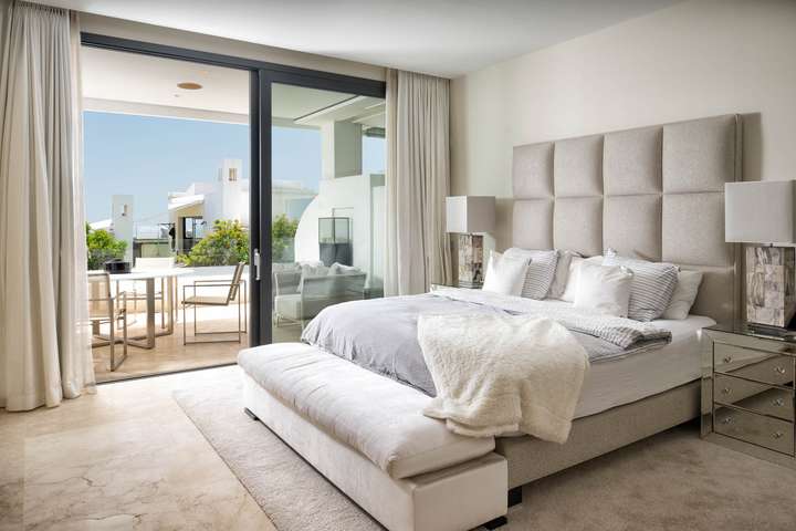 Luxurious master bedroom featuring a king-size bed, plush upholstered headboard, and direct access to a sunset-view terrace.