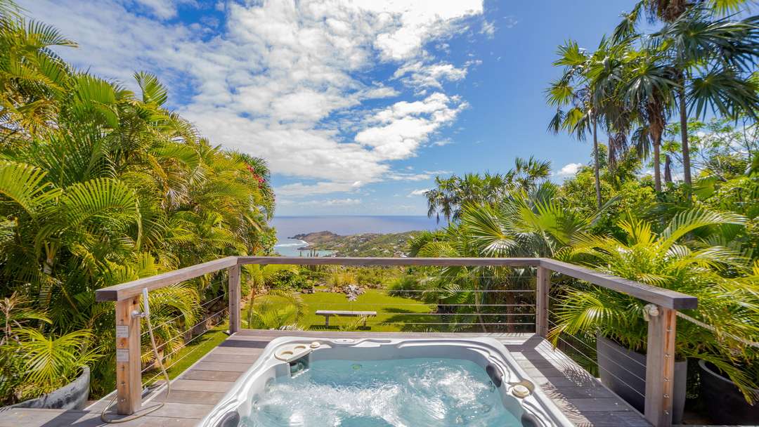 Heated jacuzzi on a wooden deck surrounded by lush tropical foliage, offering breathtaking ocean views at luxury Villa Elea.