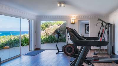 Fully equipped, air-conditioned fitness room featuring modern exercise machines and large glass doors framing lush garden views.
