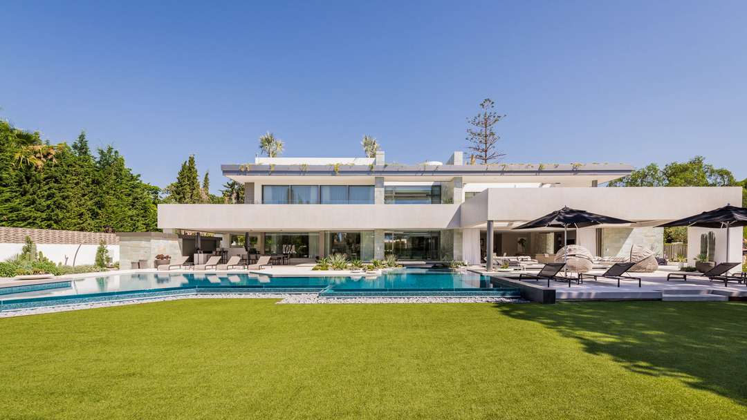 Contemporary Villa Club Mansion exterior featuring a large free-form pool, manicured lawn, and elegant outdoor lounge areas.