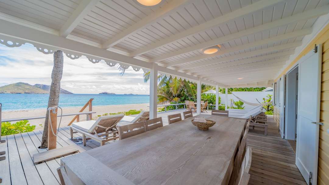 Covered al fresco dining on a beachfront terrace with a grand teak table and sweeping ocean views of Flamands Beach.