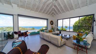 Elegant open-plan living area with whitewashed vaulted ceilings, plush seating, and expansive doors framing ocean views.