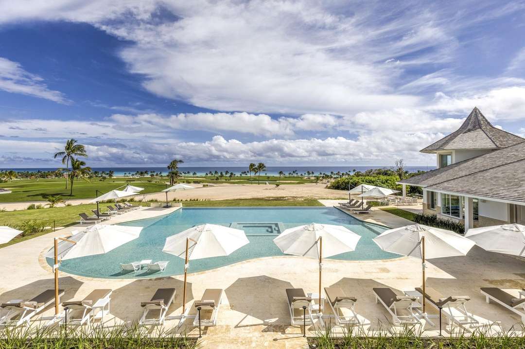 Luxury Cap Cana villa terrace featuring a private infinity pool, sun loungers, and panoramic Caribbean Sea and golf views.