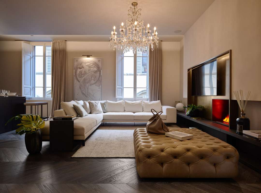 Elegant open-concept living area in Florence with an L-shaped sofa, golden-leather ottoman, and a romantic crystal chandelier.