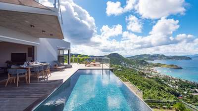 Elegant covered outdoor dining area and infinity pool on the wooden deck at Golden View, overlooking serene Lorient Bay.