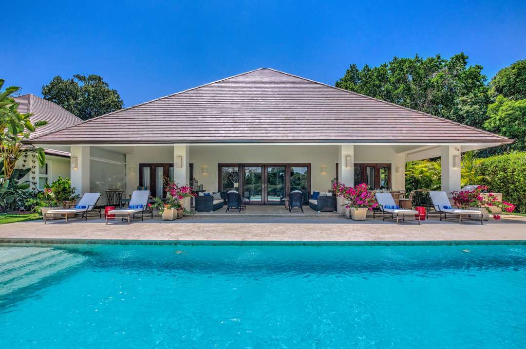 Elegant villa facade with a covered verandah, outdoor seating, and a private pool surrounded by a pristine marble terrace.