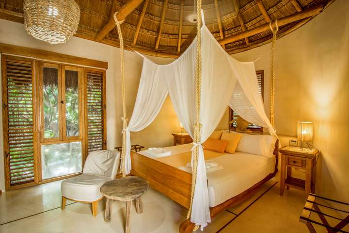 Master suite at Hacienda Chekul featuring a traditional palapa roof, king bed with canopy, and serene tropical jungle views.