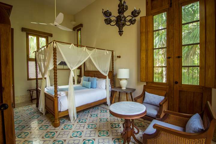 Elegant bedroom at Hacienda Chekul with a four-poster canopy bed, patterned tile floors, wooden shutters, and garden views.