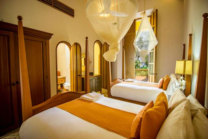 Charming bedroom at Hacienda Chekul with twin four-poster beds, elegant mosquito nets, and doors opening to a lush terrace.