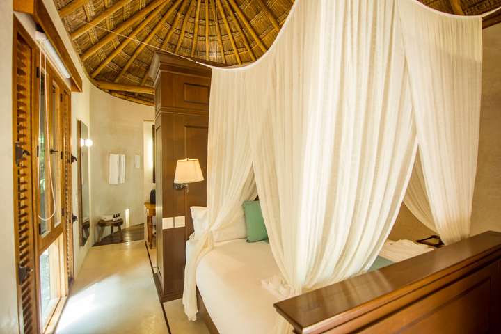 Bright luxury bedroom at Hacienda Chekul featuring a traditional palapa roof, elegant canopy bed, and rich wooden accents.