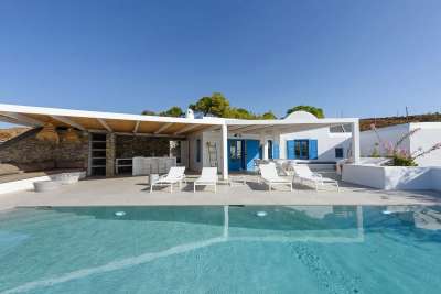 Expansive private pool terrace featuring traditional Cycladic architecture, a shaded lounge, and a built-in outdoor kitchen.
