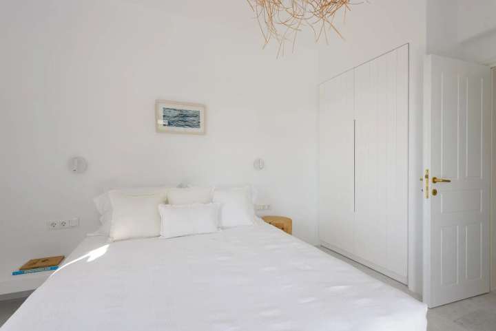 Clean, whitewashed double bedroom in our luxury Golden Beach villa with minimalist decor and a woven ceiling light.