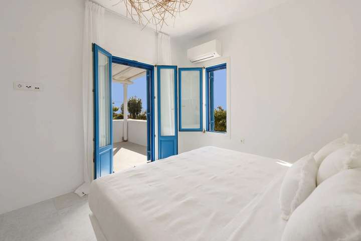 Minimalist double bedroom in a luxury Golden Beach villa featuring whitewashed surfaces and blue doors to a balcony.