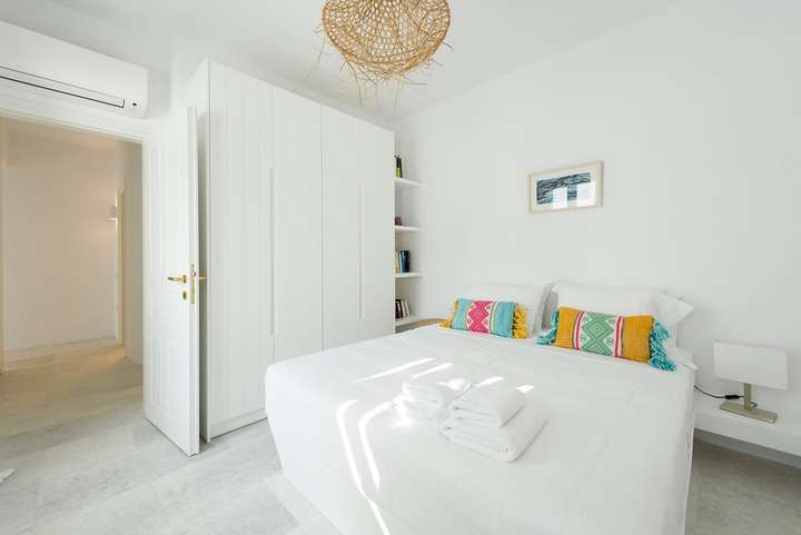 Minimalist double bedroom in our luxury Cycladic villa, featuring whitewashed surfaces and an elegant woven chandelier.