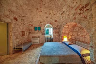 Luxury trullo bedroom featuring carved stone walls, a dome roof, comfortable double bed, and a window with nature views.