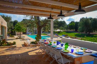 Alfresco dining terrace at Villa Hiera under a rustic pergola, overlooking the pristine private pool and lush olive groves.