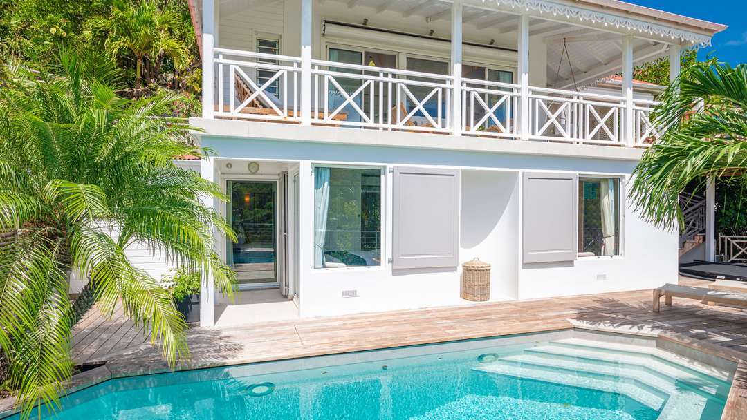 Private swimming pool and wooden sun deck at Villa Ipanema, featuring a contemporary white facade and lush tropical gardens.