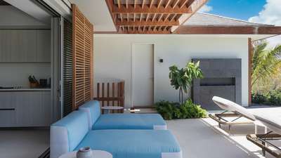 Relaxing outdoor lounge area with plush blue seating, a modern stone fireplace, and lush tropical plants at Villa Jnana.