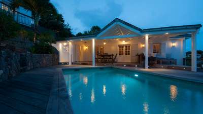 Villa Kiara's inviting heated pool and wooden terrace at dusk, highlighting the elegant covered outdoor dining and lounge area.