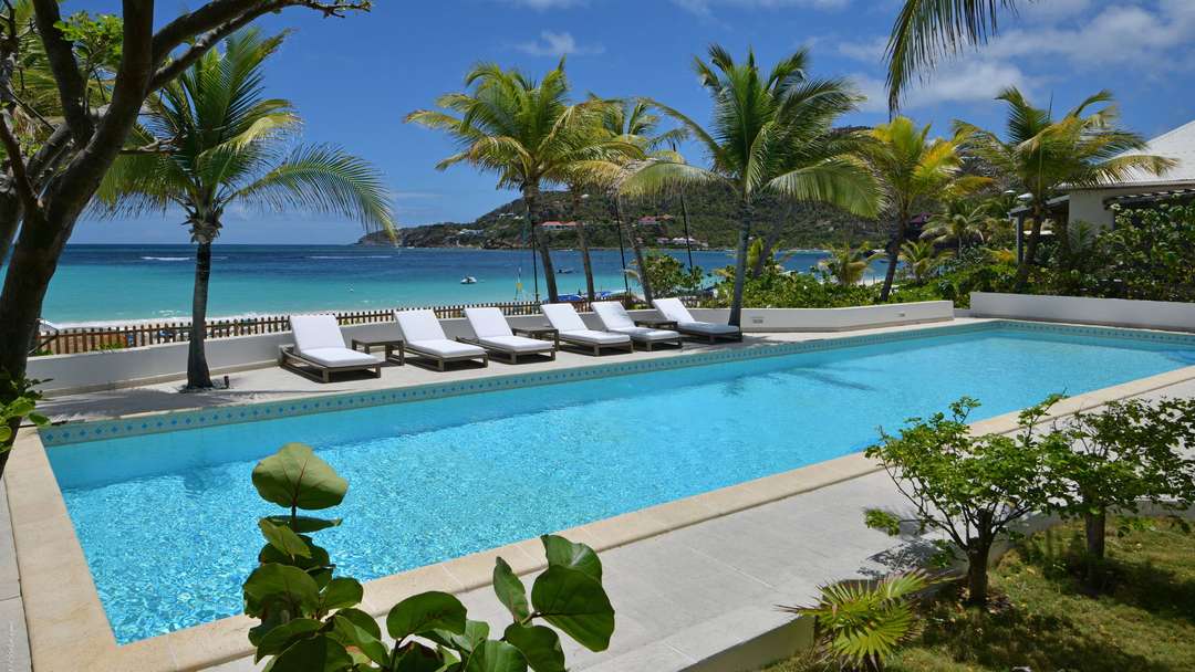 Heated private pool at Villa Kumara featuring elegant white sun loungers, palm trees, and breathtaking St-Jean beach views.