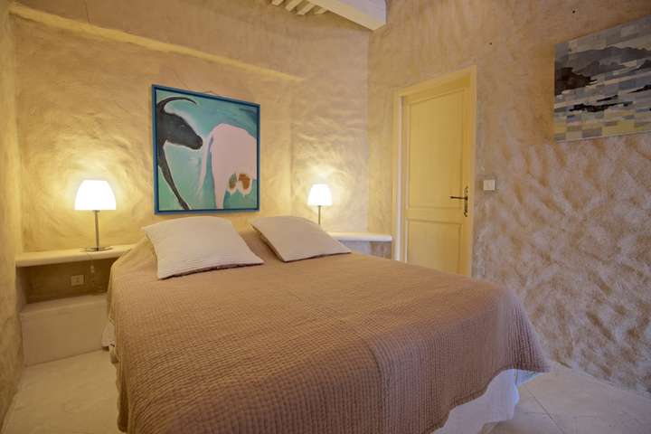 Elegant bedroom at La Citadelle featuring textured stone walls, a plush queen bed, and unique artwork for a tranquil retreat.