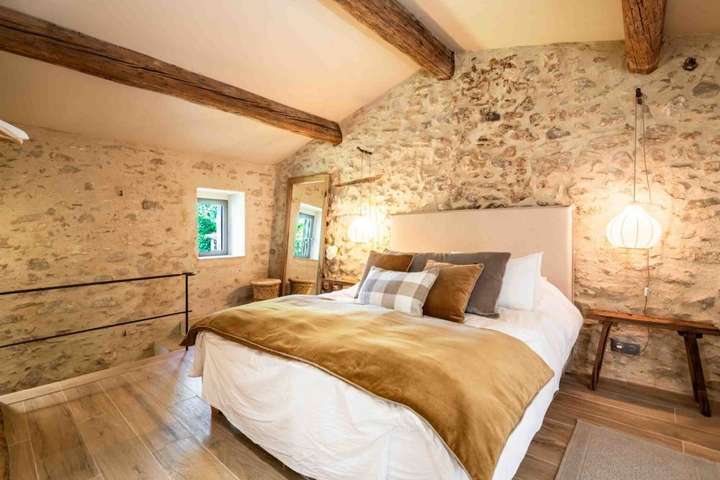 Cozy second bedroom with exposed wooden beams, authentic stone walls, and luxurious bedding in this Provençal villa.