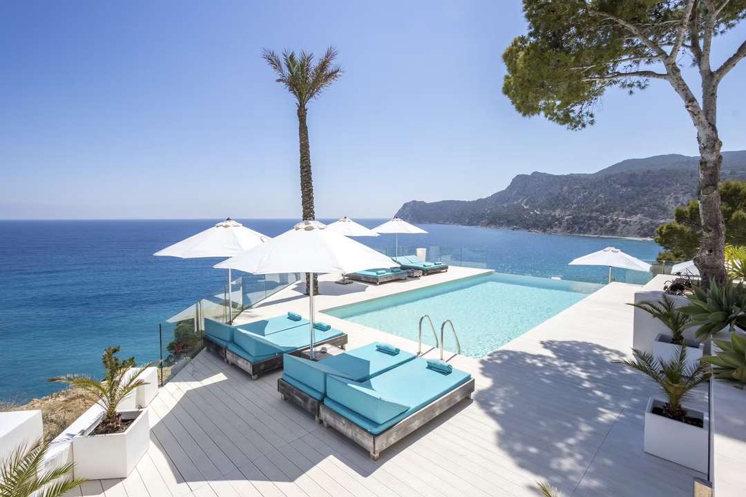 Infinity pool at La Villa Es Cubells with white loungers, blue cushions, and panoramic Mediterranean Sea views in Ibiza.