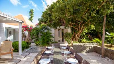 Beautifully set glass-topped outdoor dining table on a spacious terrace, surrounded by vibrant tropical gardens in St Barts.