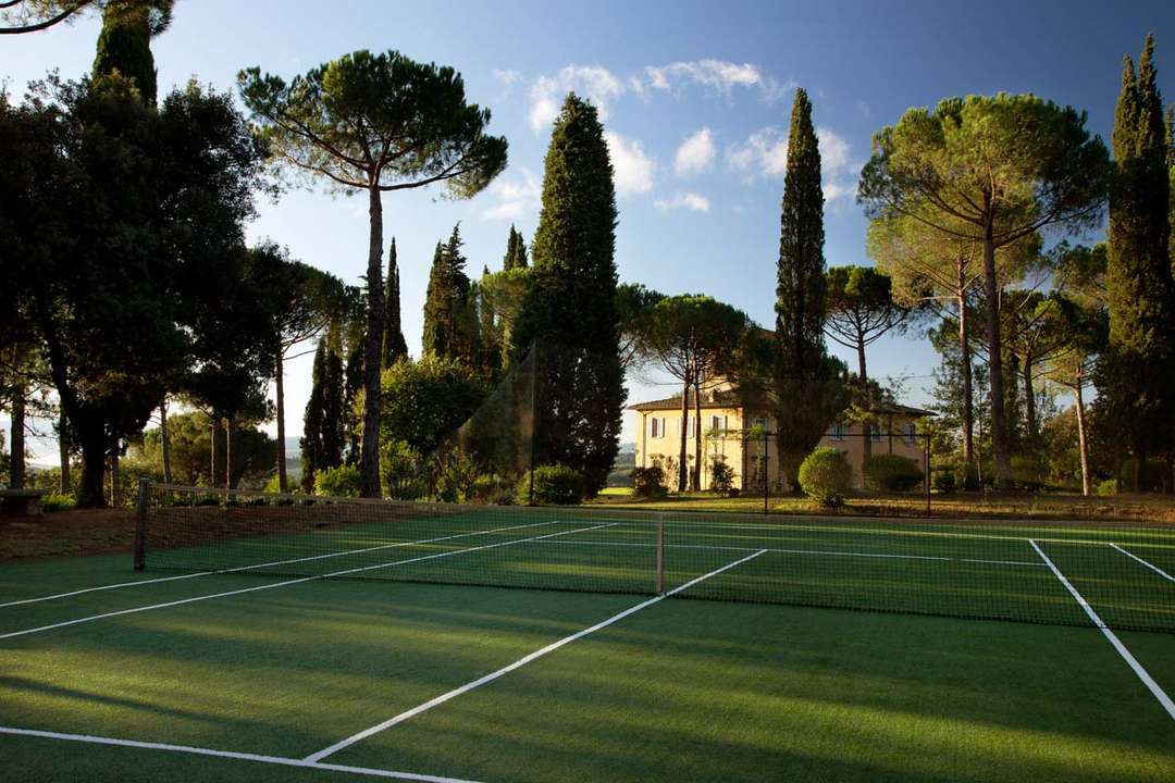 Private tennis court surrounded by cypress trees at a luxury Chianti villa estate near Florence.