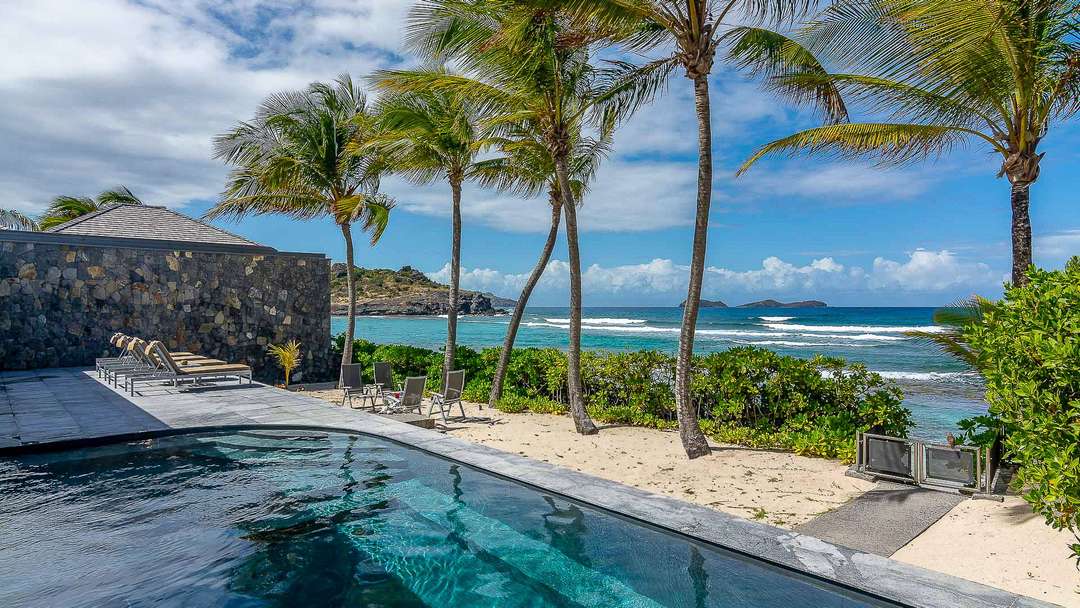 Sparkling private pool at Villa Les Basses, framed by palm trees and a sandy path to Lorient beach with stunning ocean views.