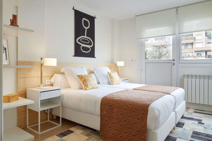 Bright twin bedroom at Echoes of Ondarreta featuring crisp white linens, modern art, and direct access to a private balcony.
