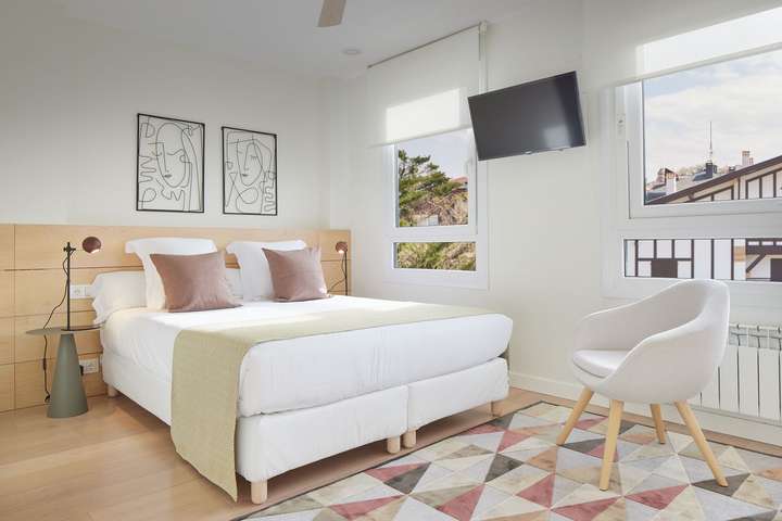 Bright en-suite bedroom with plush bedding, light wood accents, a Smart TV, and serene views in our San Sebastián retreat.
