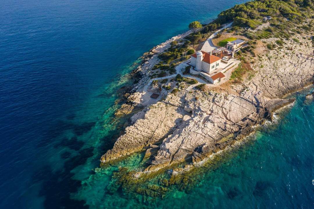 Aerial view of Villa Lighthouse Ligero on a secluded islet, featuring rocky shores and crystal-clear Adriatic Sea waters.