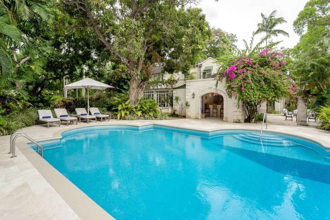 Large private pool at Maddox villa in Barbados, featuring coral stone architecture, lush gardens, and a poolside bar.