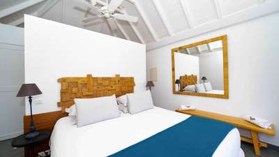 Luxury St. Barths villa bedroom featuring a plush king-size bed, unique wooden headboard, and a classic vaulted ceiling.