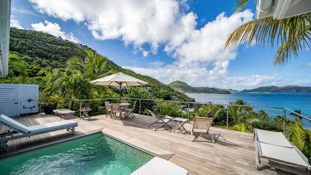 Expansive wooden terrace with a private pool, sun loungers, and alfresco dining offering panoramic ocean views in St Barths.