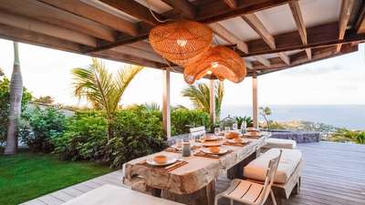 Luxury outdoor dining terrace at Villa Mamiami with a large wooden table, cushioned benches, and breathtaking ocean views.