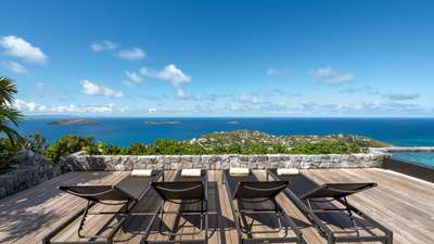 Comfortable sun loungers on a serene private terrace with stone accents, offering panoramic ocean vistas for a luxury escape.